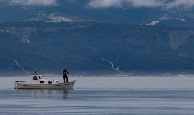 Schöner Schuss eines Mannes auf einem Boot, das Fisch im See mit Bergen im Hintergrund fängt