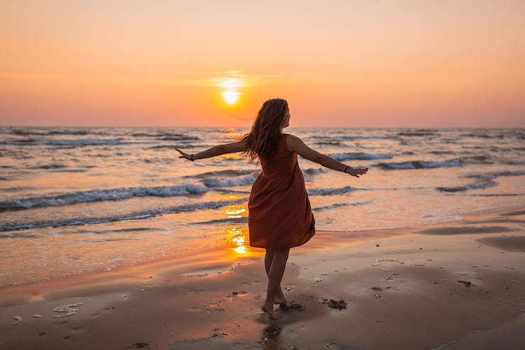 Kostenlose Foto schöner schuss eines modells, das ein braunes sommerkleid trägt, das den sonnenuntergang am strand genießt