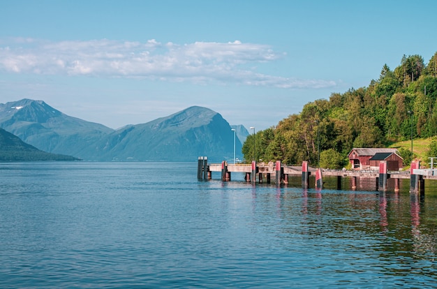 Schöner Schuss eines Piers auf dem Meer nahe einem Baumwald, der durch hohe Berge in Norwegen umgeben ist