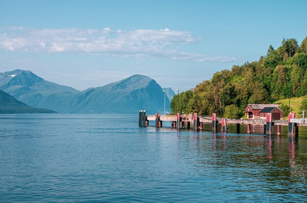 Schöner Schuss eines Piers auf dem Meer nahe einem Baumwald, der durch hohe Berge in Norwegen umgeben ist