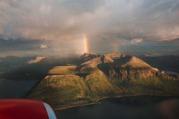 Schöner schuss eines regenbogens über grünen bergen unter einem bewölkten himmel