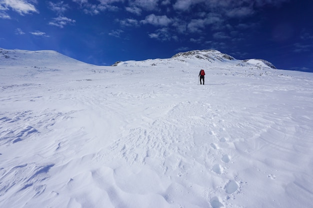 Schöner Schuss eines Wanderers mit einem roten Reiserucksack, der einen Berg unter dem blauen Himmel wandert