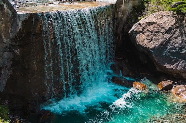 Schöner Schuss eines Wasserfalls nahe riesigen Felsformationen in Pragelato, Italien