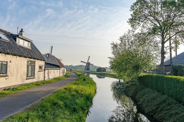 Schöner Schuss eines Wasserkanals an der Seite einer schmalen Straße mit einer Windmühle auf einem Feld