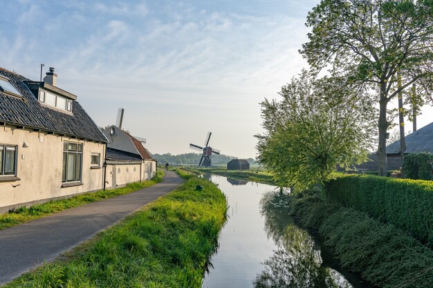 Schöner Schuss eines Wasserkanals an der Seite einer schmalen Straße mit einer Windmühle auf einem Feld