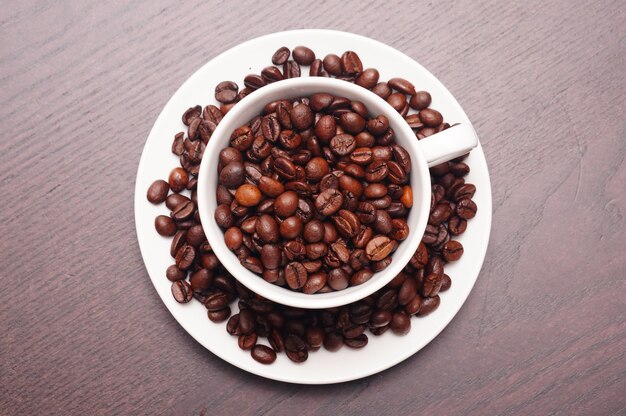 Schöner Schuss von Kaffeebohnen in der weißen Tasse und im Teller auf einem Holztisch