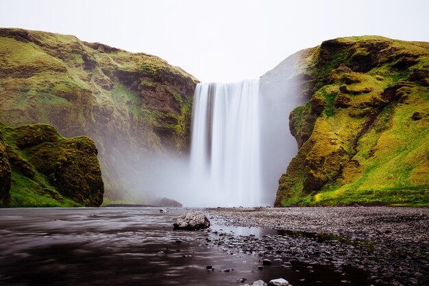 Schöner Wasserfall zwischen grünen Hügeln in Skogafoss, Island