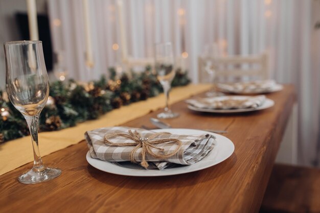 Schöner Weihnachtsserviertisch mit Kerzen und Tannenbaumdekoration in gemütlicher, moderner Innenaufnahme. Feiern Sie das neue Jahr im Dezember, umgeben von saisonal dekorierten Gläsern und Tellern