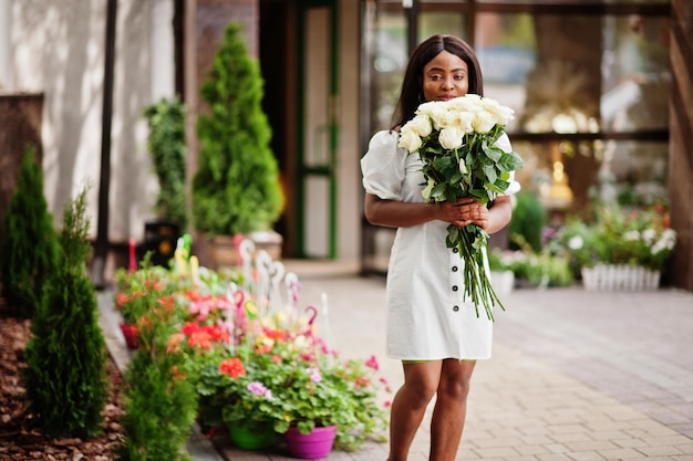 Schönes afrikanisch-amerikanisches Mädchen, das einen Strauß weißer Rosen hält, blüht bei der Datierung in der Stadt Schwarze Geschäftsfrau mit Blumenstrauß