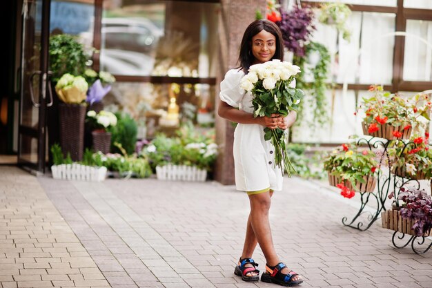 Schönes afrikanisch-amerikanisches Mädchen, das einen Strauß weißer Rosen hält, blüht bei der Datierung in der Stadt Schwarze Geschäftsfrau mit Blumenstrauß