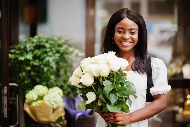 Schönes afrikanisch-amerikanisches Mädchen, das einen Strauß weißer Rosen hält, blüht bei der Datierung in der Stadt Schwarze Geschäftsfrau mit Blumenstrauß