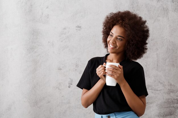 Schönes afrikanisches Mädchen, das Tasse über Lichtwand hält.