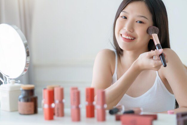 Schönes asiatisches Frauen-Weiß-T-Shirt-Lächeln mit Glückshandgriff erröten an und Make-up-Kosmetikartikel im Schlafzimmer mit gesundem Gesichtshautpflegekonzept