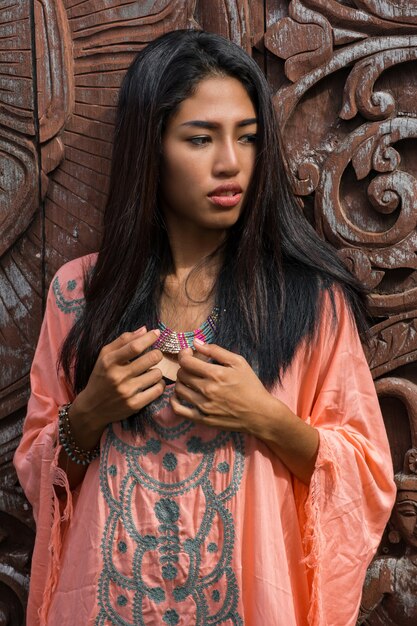 Schönes asiatisches Modell im rosa Boho-Kleid, das über Zierwand des Holzes aufwirft.