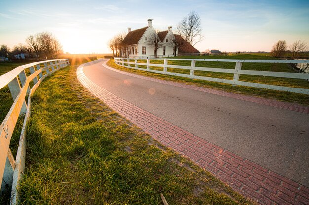 Schönes Bild einer Straße mit weißen Zäunen neben dem Haus bei Sonnenuntergang
