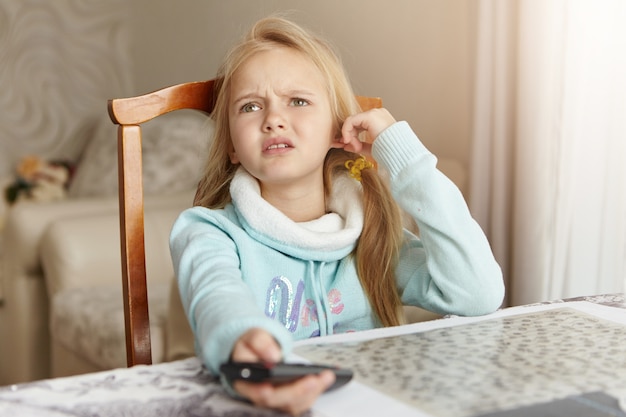 Schönes blondes kaukasisches kleines Mädchen, das auf Stuhl im Wohnzimmer sitzt