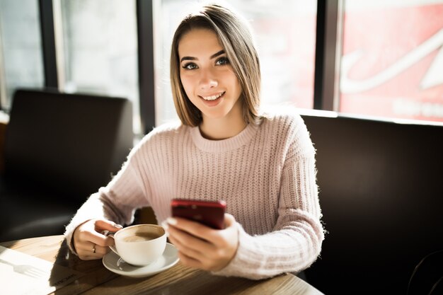 Schönes blondes Mädchen, das ihr Handy im Café während der täglichen Kaffeepause-Mittagspause verwendet