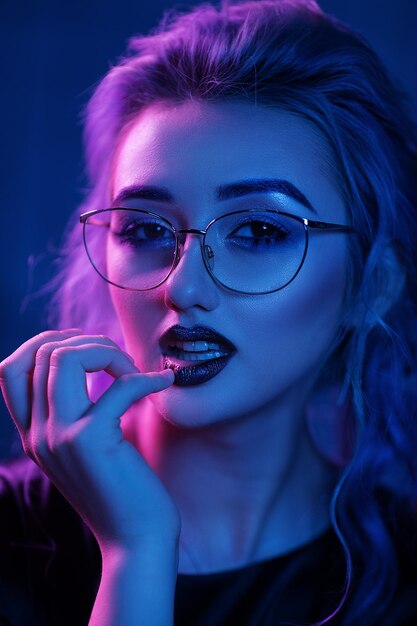Schönes blondes Mädchen in den Gläsern Sexy, die helle Lippen berühren. Aufstellung im blauen Licht.