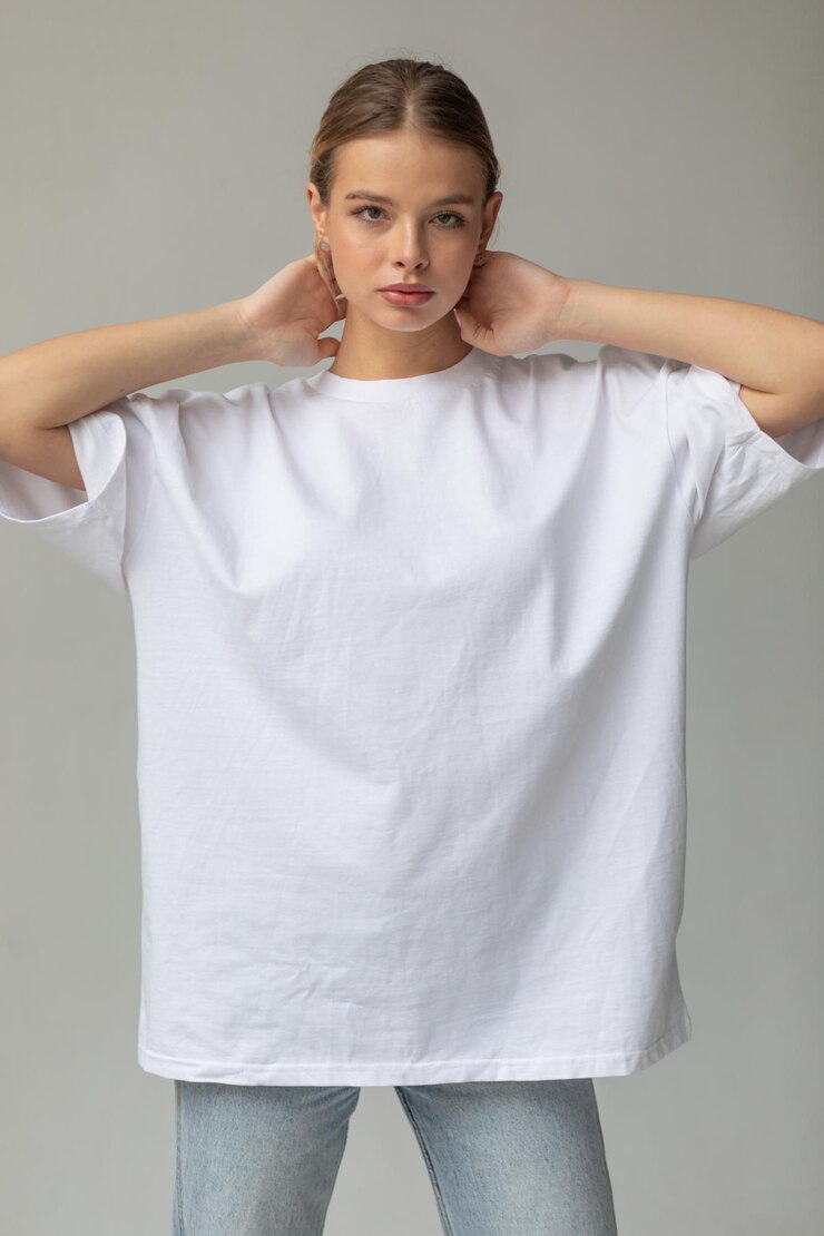 Schönes blondes Mädchen in einem weißen übergroßen T-Shirt und blauen Jeans posiert auf einem grauen Hintergrund