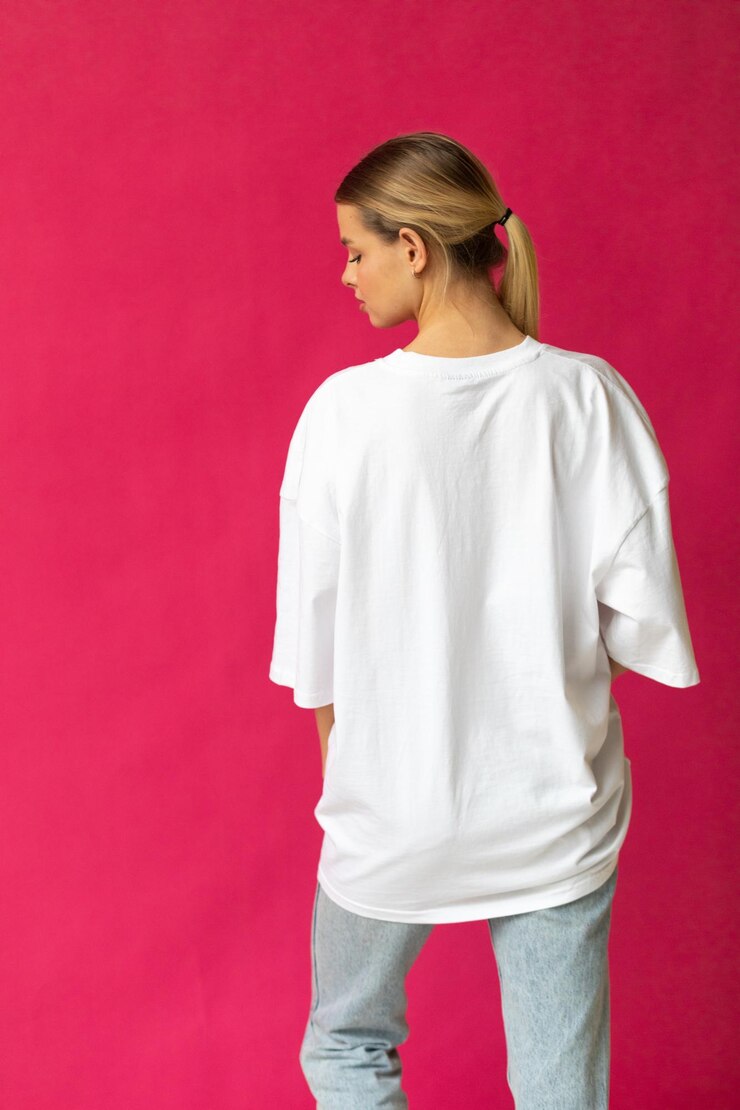 Schönes blondes Mädchen in einem weißen übergroßen T-Shirt und blauen Jeans posiert auf einem grauen Hintergrund