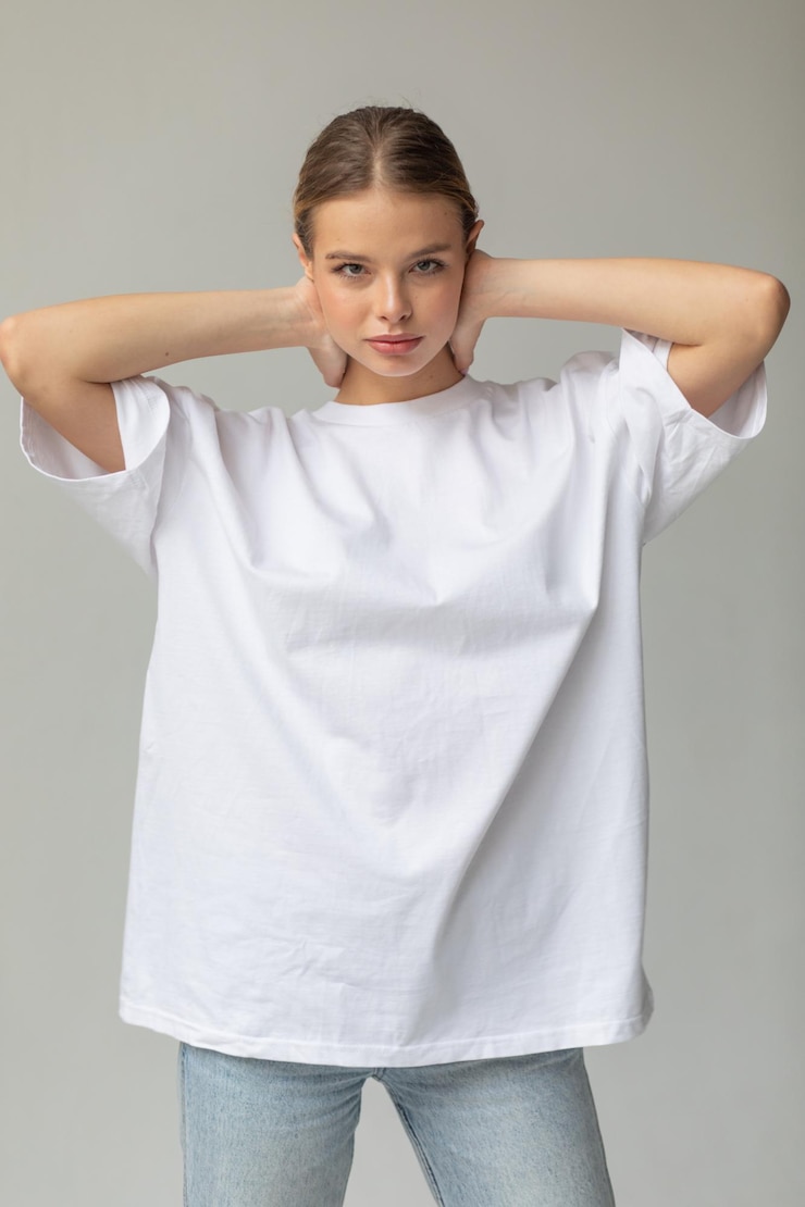 Schönes blondes Mädchen in einem weißen übergroßen T-Shirt und blauen Jeans posiert auf einem grauen Hintergrund