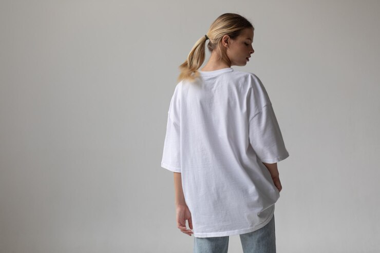 Schönes blondes Mädchen in einem weißen übergroßen T-Shirt und blauen Jeans posiert auf einem grauen Hintergrund