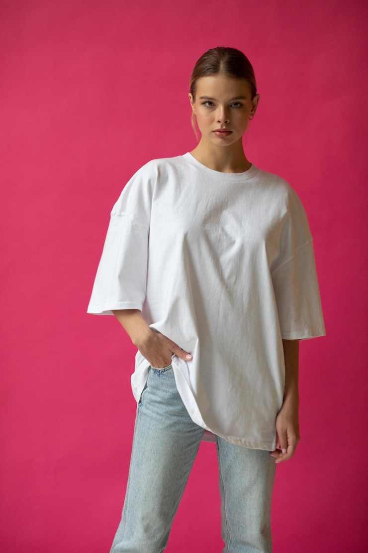 Schönes blondes Mädchen in einem weißen übergroßen T-Shirt und blauen Jeans posiert auf einem grauen Hintergrund