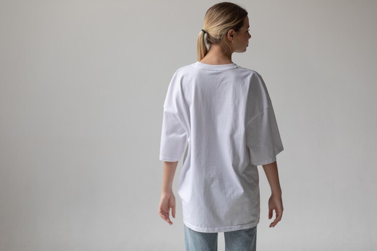 Schönes blondes Mädchen in einem weißen übergroßen T-Shirt und blauen Jeans posiert auf einem grauen Hintergrund