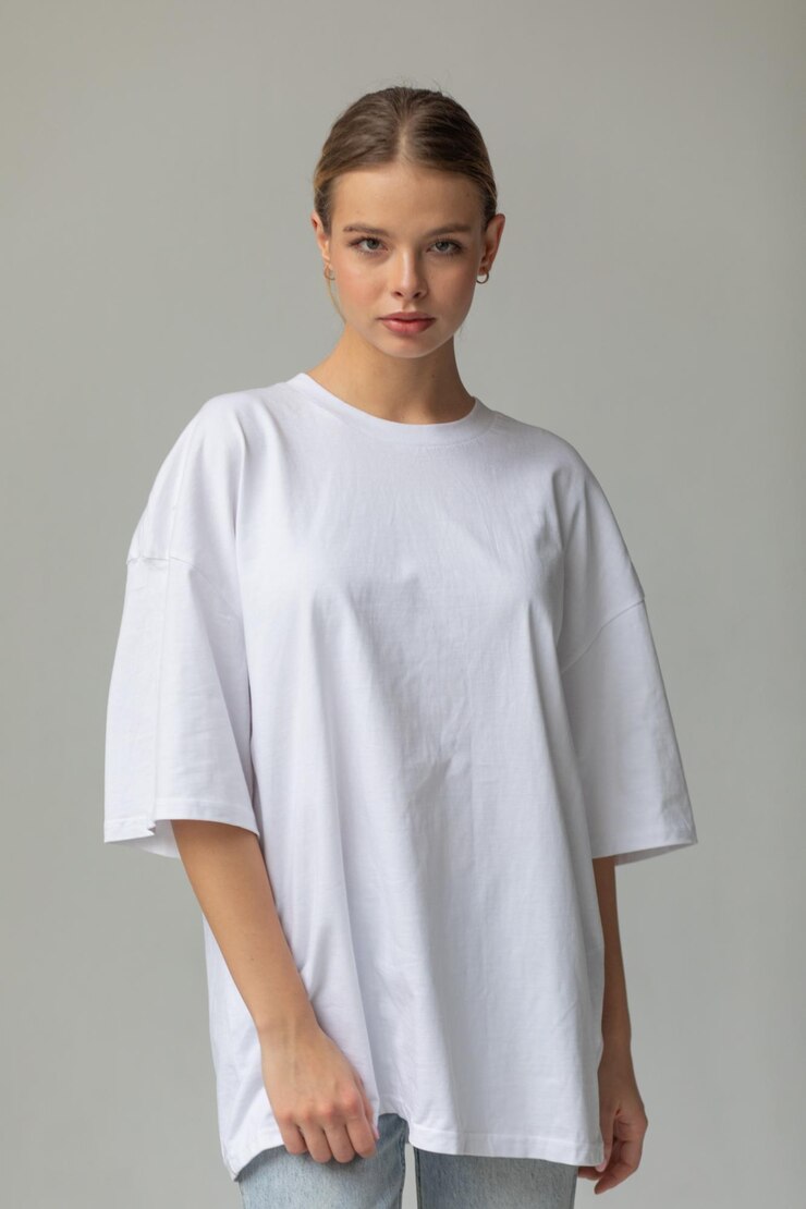 Schönes blondes Mädchen in einem weißen übergroßen T-Shirt und blauen Jeans posiert auf einem grauen Hintergrund