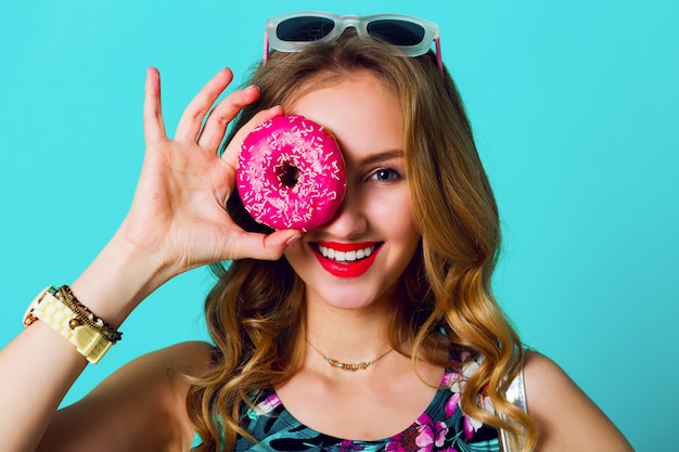 Schönes blondes Modemodellmädchen, das bunte rosa Donuts nimmt. Lustige freudige Frau mit Süßigkeiten, Nachtisch. Diät, Diätkonzept. Junk Food. Helle Farben.