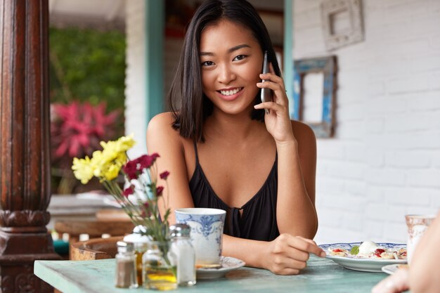 schönes chinesisches Frauenporträt, das mit Smartphone auf einem Café spricht