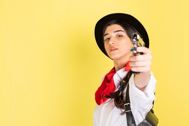 Schönes Cowgirl mit Waffe und Blick auf die Kamera auf gelbem Hintergrund Hochwertiges Foto