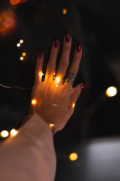 Schönes dunkles Foto der Handfinger der Frau mit großem silbernem Ring auf Blumen und leuchtenden Lichtern
