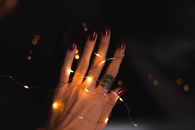 Schönes dunkles Foto der Handfinger der Frau mit großem silbernem Ring auf Blumen und leuchtenden Lichtern