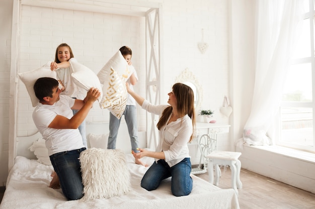 Schönes Elternteil mit ihrem Kind, das Kissenschlacht auf Bett im Schlafzimmer spielt