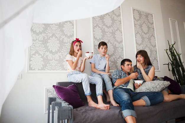 Schönes Elternteil und ihre Kinder, die Erdbeere beim Sitzen auf Sofa essen