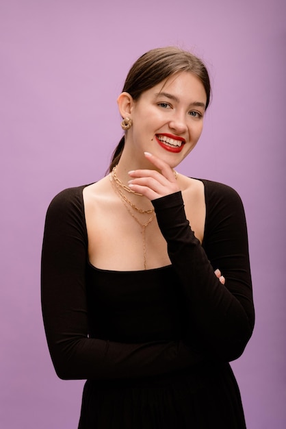 Schönes europäisches junges brünettes mädchen mit perfektem lächeln und roten lippen im schwarzen pullover blickt auf violettem hintergrund in die kamera