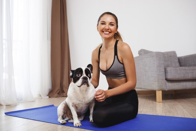 Schönes Fitnessmädchen, das auf Boden mit Hund sitzt