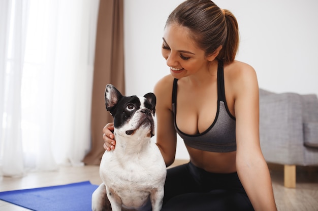 Schönes Fitnessmädchen, das auf Boden mit Hund sitzt