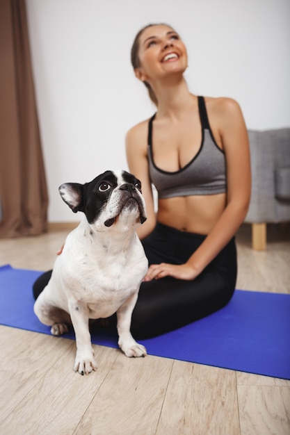 Schönes Fitnessmädchen, das auf Boden mit Hund sitzt