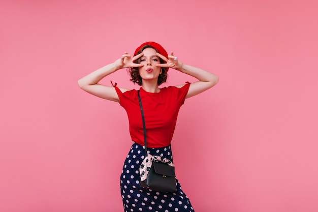 Schönes französisches weibliches Modell in der Baskenmütze, die Spaß hat. Innenporträt der blithesome europäischen Frau in den roten Kleidern.