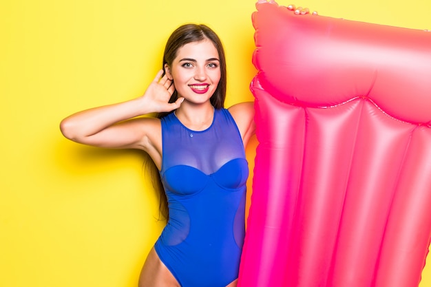 Schönes fröhliches Mädchen in einem hellen Badeanzug mit einer Luftmatratze auf einer gelben Wand.