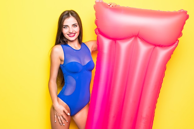 Schönes fröhliches Mädchen in einem hellen Badeanzug mit einer Luftmatratze auf einer gelben Wand.