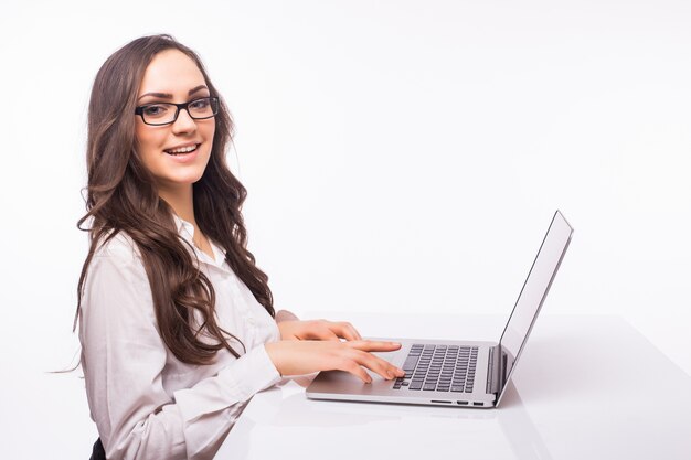 Schönes Geschäftsfrauenlächeln, das am Schreibtisch arbeitet und Laptop verwendet, der Bildschirm betrachtet, Handschrift, lokalisiert über weißer Wand