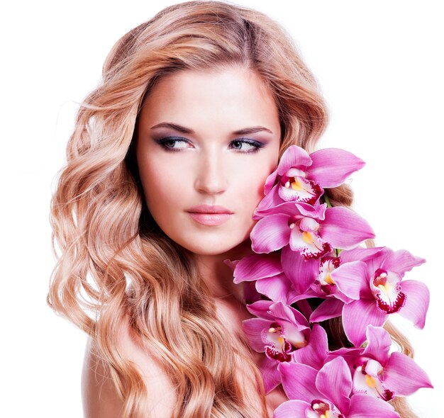 Schönes Gesicht der jungen blonden Frau mit gesunden Haaren und rosa Blumen nahe Gesicht - lokalisiert auf Weiß.