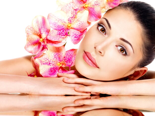 Schönes Gesicht der jungen hübschen Frau mit gesunder Haut und rosa Blumen - lokalisiert auf Weiß