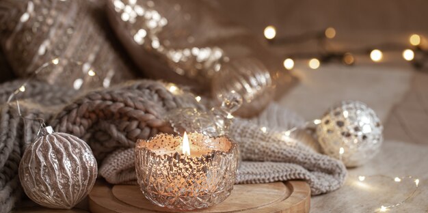 Schönes glänzendes silbernes Weihnachtsdekor und brennende Kerze nah oben. Gemütliche Winteratmosphäre.