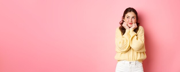 Schönes Glamour-Mädchen, das an die Liebe denkt und nach oben schaut und Tagträume vorstellt, die sich etwas Süßes und Romantisches vorstellen, das vor rosa Hintergrund steht