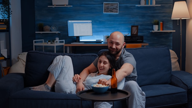 Schönes glückliches Paar vor dem Fernseher auf der Couch, die nachts lachend entspannt