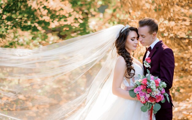 Schönes Hochzeitspaar im Wald mit vergilbten Bäumen, die fast küssen, Ehekonzept, Hochzeitspaar im Herbstwald